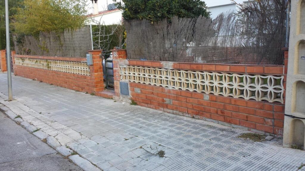 Muro de cerramiento exterior antes de la rehabilitación, con ladrillo visto y celosía antigua en Calafell.